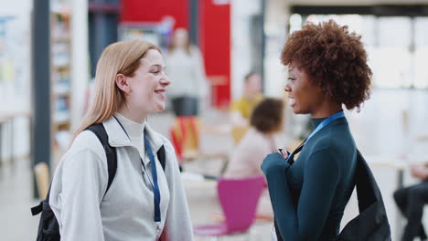 two female college student friends meeting and looking at mobile phone in communal campus building