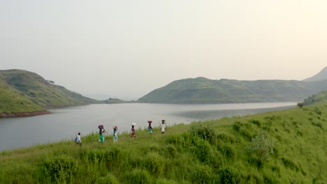 aerial view of people walking in the hills with bag on their head near calm lake at early morning in india