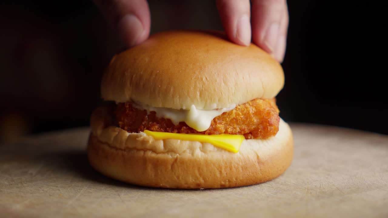 Mettere il panino su un hamburger di pesce fritto spalmato con maionese e formaggio.