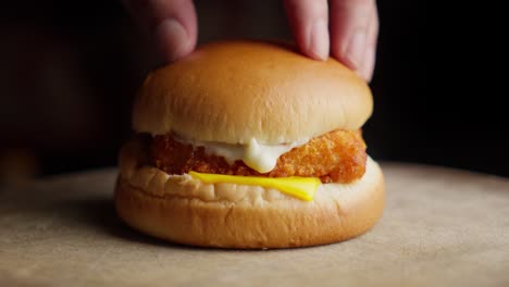 putting bun on fried fish burger spread with mayonnaise and cheese