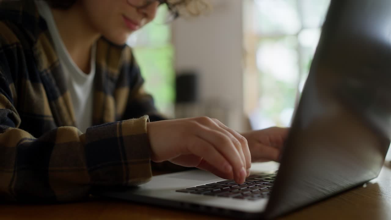 un primer plano de una estudiante feliz en una camisa a cuadros escribiendo en un teclado de portátil mientras está sentada en una mesa en la universidad