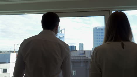 Two-businesspeople-go-to-window-in-the-office