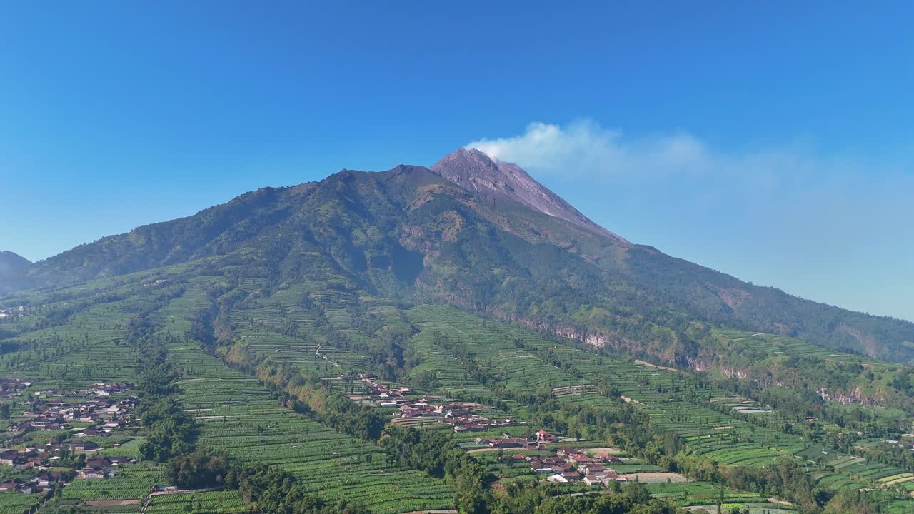 Scenic aerial rural landscape featuring volcanic mountain with smoke rising from the crater. Mount Merapi Volcano, Indonesia