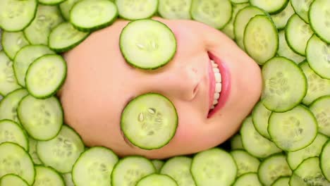 smiling womans face surrounded by cucumber slices