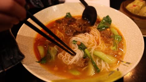 persona disfrutando de sopa de fideos china con palillos