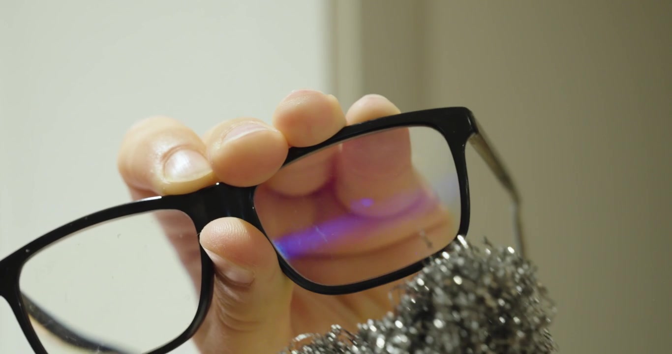 Close-up of a person incorrectly cleaning eyeglass lenses with abrasive steel wool, illustrating improper lens care, scratches, and damaged eyewear.