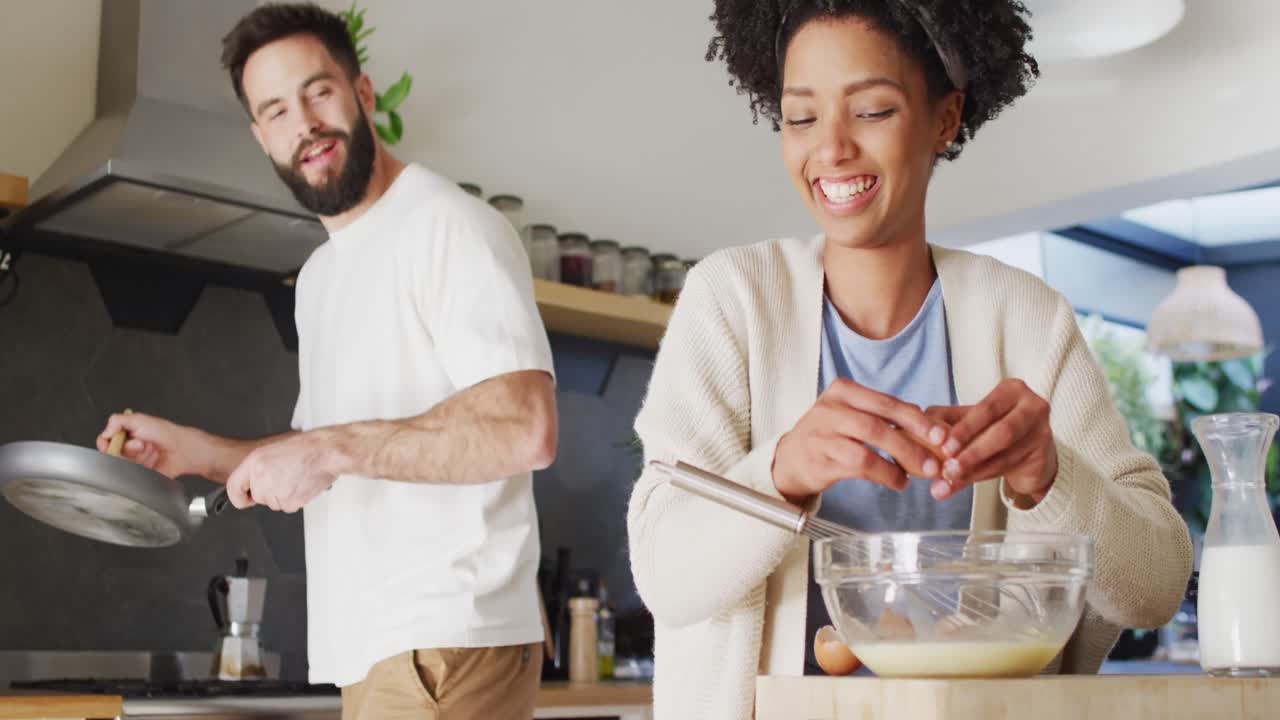 video de una feliz pareja diversa riendo y cocinando el desayuno en la cocina, con espacio para copiar