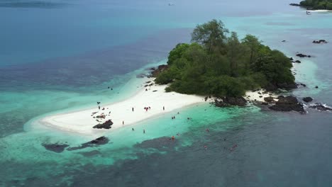 Vista-Aérea-De-Personas-En-Una-Pequeña-Isla-Tropical-Con-árboles,-Playas-Rocosas-Y-De-Arena-Blanca-En-Medio-Del-Océano