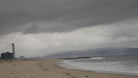 waves crash onto an empty beach on a foggy day, storm approaching