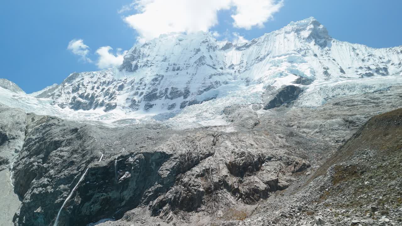 Slow aerial approach reveals the brilliant turquoise Laguna 69, then tilts up to showcase the majestic snow-capped Cordillera Blanca mountains in Huascarán National Park, Peru