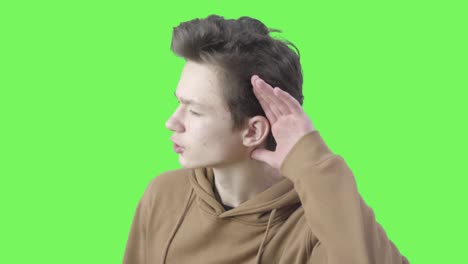 side view of brunette boy holding hand to ear and approaching to camera. portrait of caucasian male teenager listening to something at green screen background. chromakey, attention, trouble hearing.