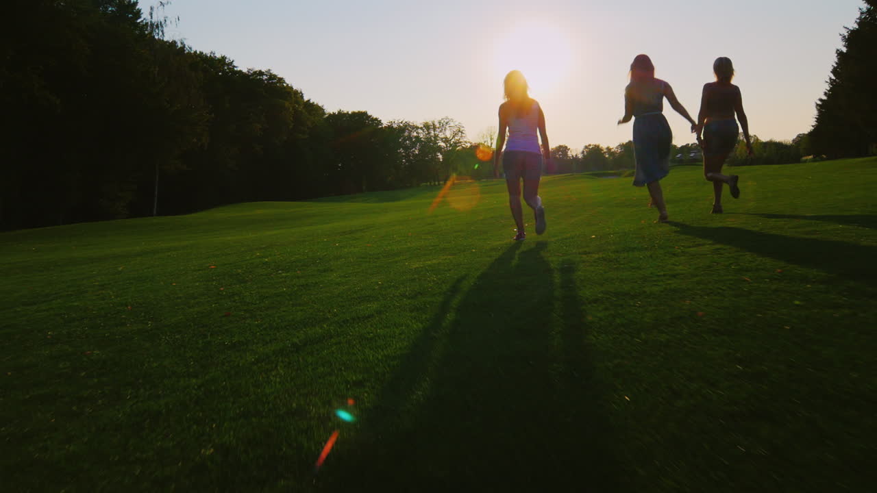 해질녘에 잔디밭에서 달리는 평온한 젊은 여성들의 실루엣