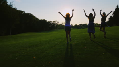 Silhouetten-Von-Unbeschwerten-Jungen-Frauen,-Die-Bei-Sonnenuntergang-Auf-Dem-Rasen-Laufen