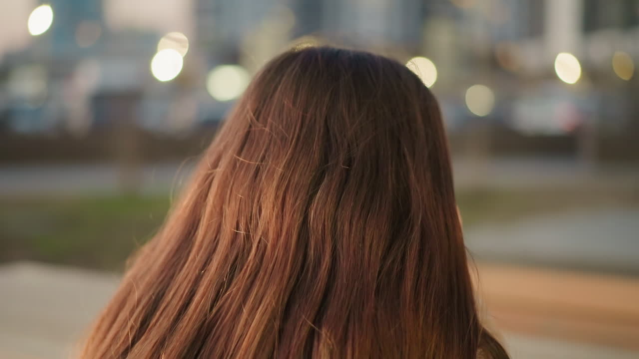 A close-up back shot of a woman with long brown hair, set against a softly blurred urban background. quiet elegance of the scene, focusing on the texture and color of the hair