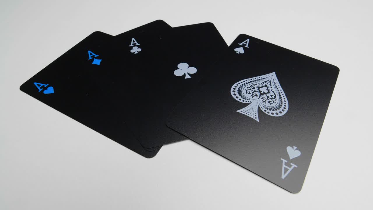 Orbit shot of the four aces on a white surface of a deck of black cards