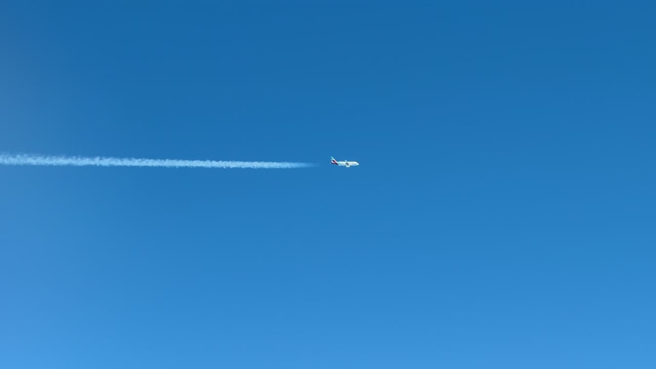 A twin-engine Jet and its contrail crossing horizontally a blue sky. Aerial footage taken from another jet cockpit flying bellow a parallel track