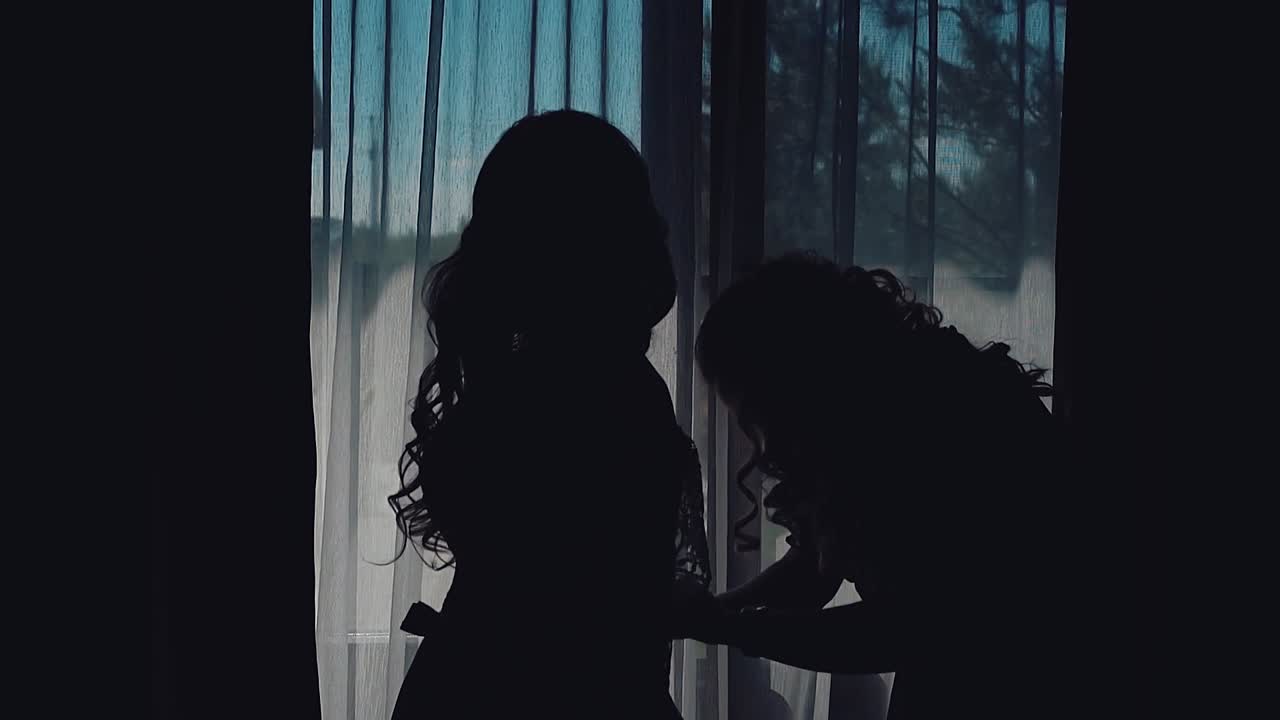 Bride's girl-friend helps the bride put on a wedding dress