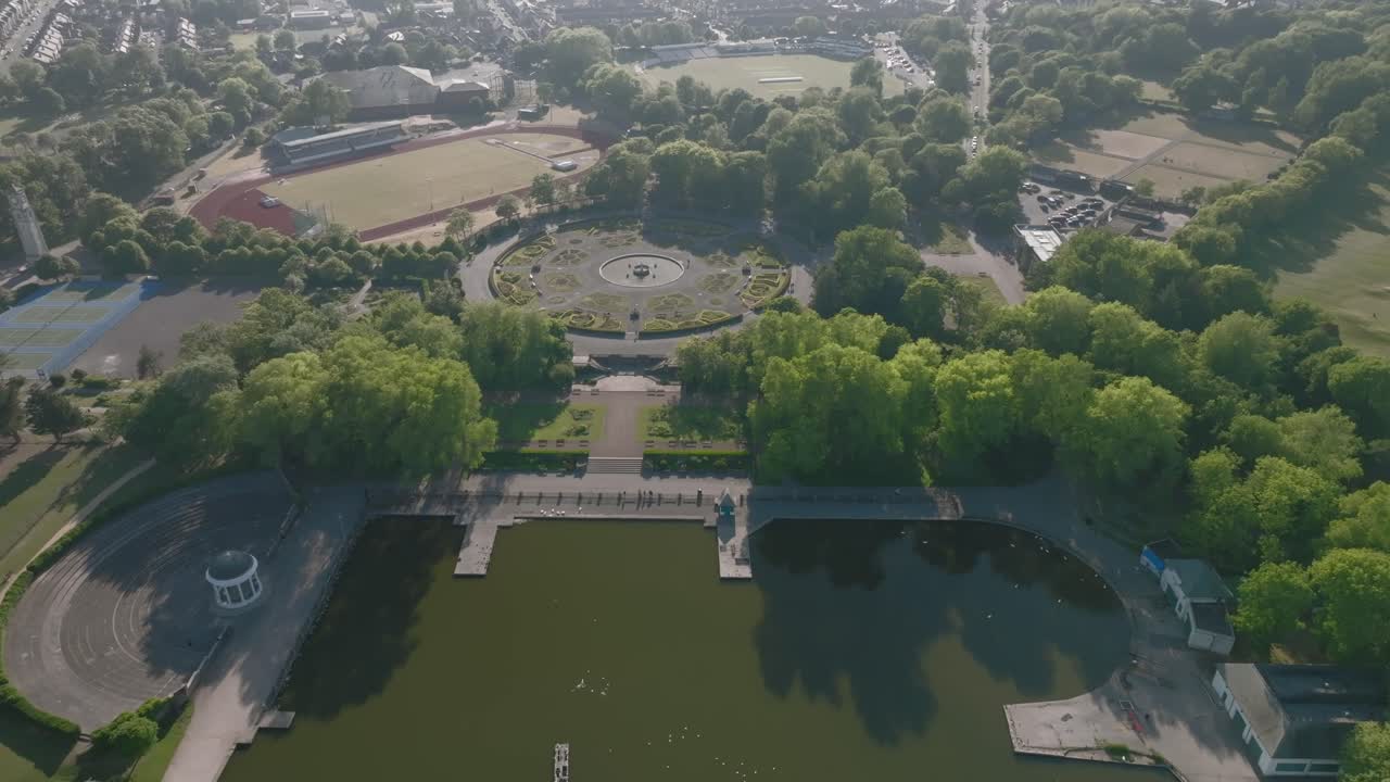 Parkland lake and circular Italian style gardens next to running track in suburban setting on sunny day. Stanley Park, Blackpool, Lancashire, UK.