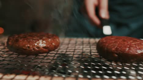 close up on burger patties being fried on hot, smoky grill