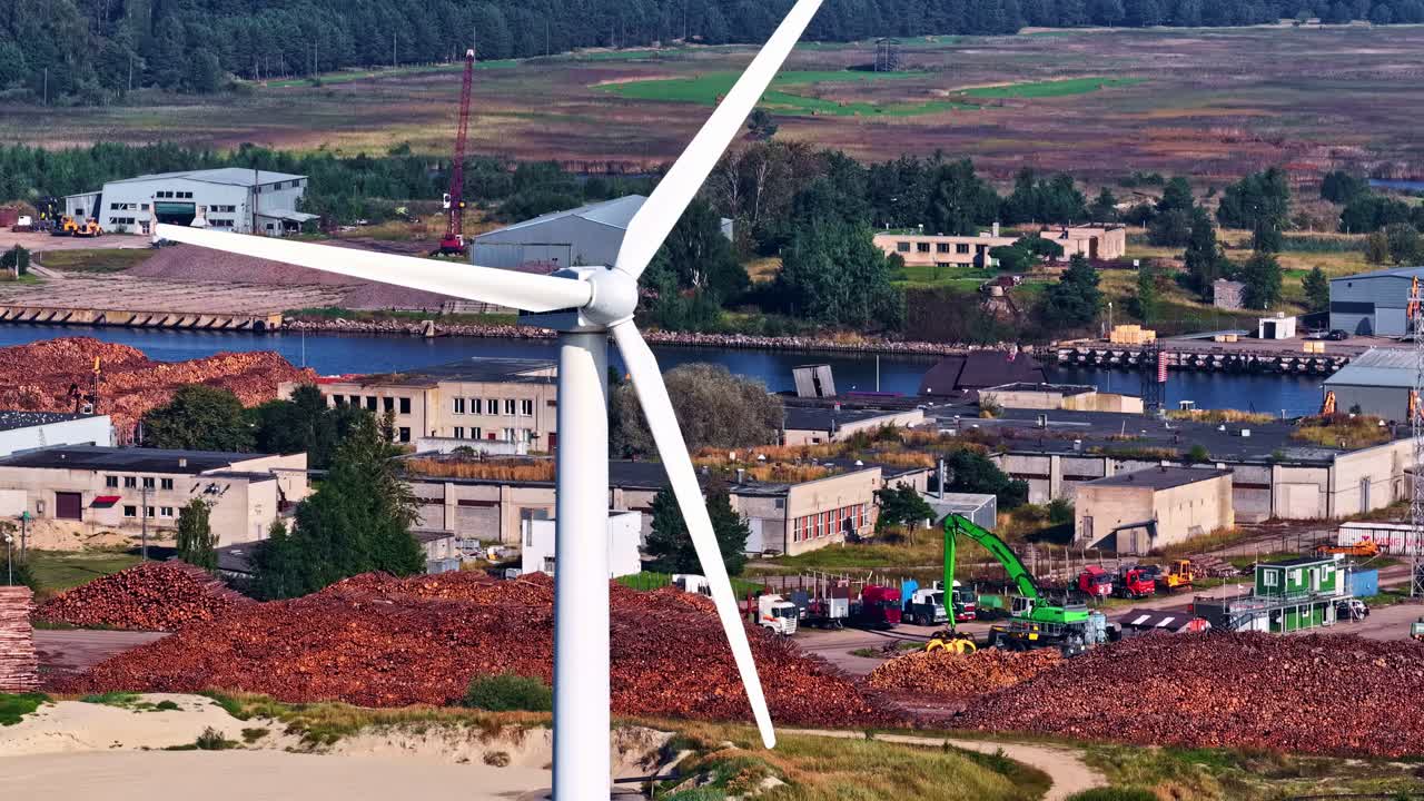 A windmill in motion stands before an industrial backdrop, blending energy and machinery