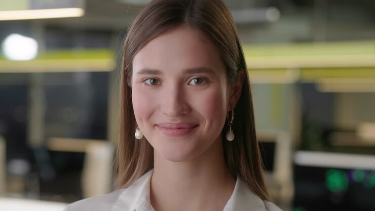 Front view of beautiful young Woman professional Wearing White Shirt. Portrait of young female office manager looking to camera and having good mood. Blurred office background