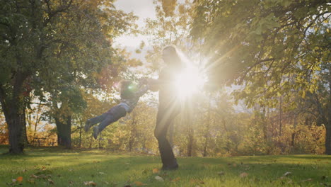 A-happy-young-mother-circles-her-child,-has-a-good-time-together-on-a-walk.-Against-the-backdrop-of-sunset