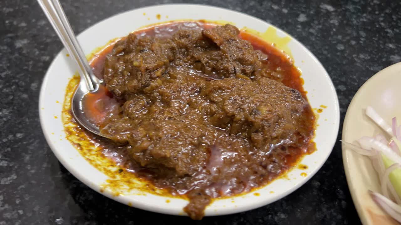 Oily Mutton kossa served in a classic white plate in an old restaurant in Kolkata.