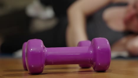 primer plano de pesas moradas en el suelo durante una persona femenina haciendo ejercicio en segundo plano