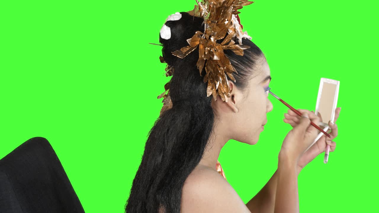 Dançarina balinesa maquiando as pálpebras em estúdio
