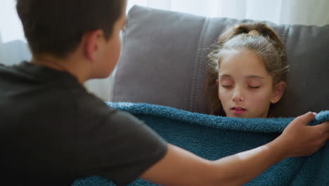 young boy gently covering his sister with a soft fluffy blanket as she sleeps deeply on the couch, the serene moment is highlighted by natural light filtering through the window
