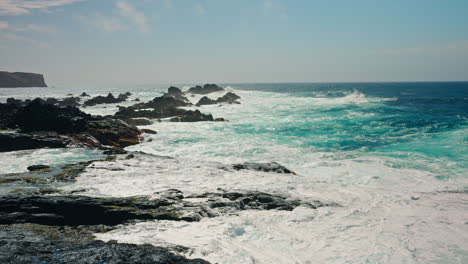 slow motion shot of rough ocean waves crushing against the volcanic rocky coastline