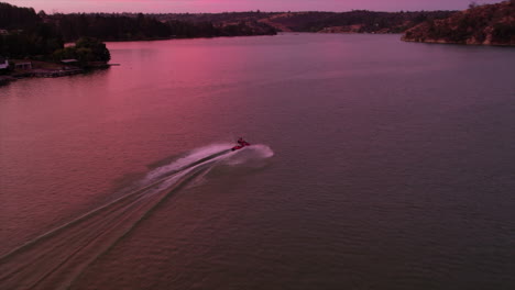 jet ski speeding across lake with pink sunlight reflected on surface