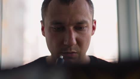 Man-smokes-e-cigarette-looking-at-laptop-screen-in-office