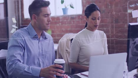 Animation-of-data-processing-over-diverse-man-and-woman-discussing-over-a-laptop-at-office