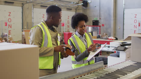 african american male and female workers with clipboard next to conveyor belt in warehouse