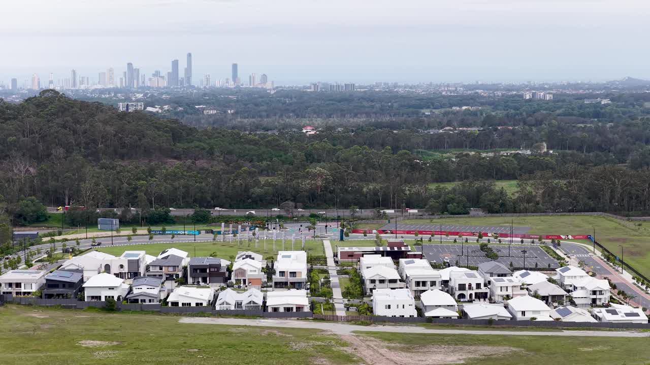 Drone camera slowly descends over modern suburban homes, revealing forest, mountains, and distant skyline