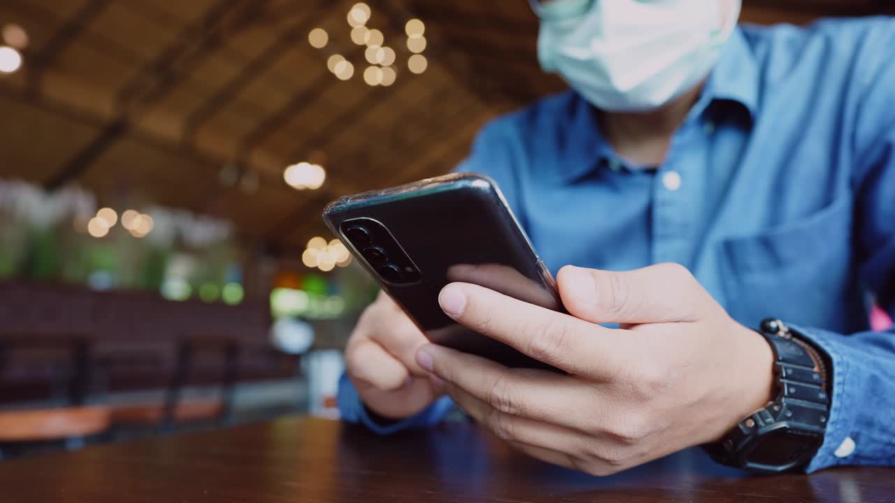 un joven empresario con una máscara quirúrgica está tomando una videoconferencia con los clientes a través de un teléfono inteligente conectado a internet.