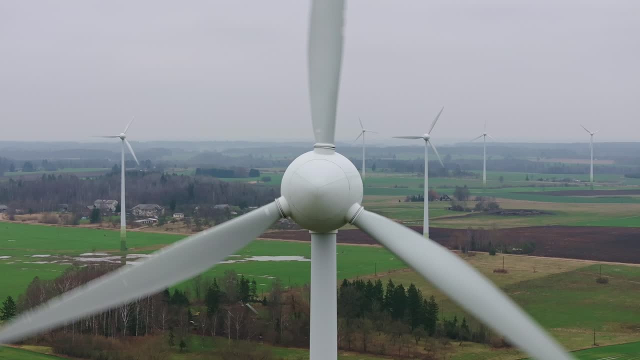 Wind turbines blades spinning in strong winds over a green spring landscape, 4K