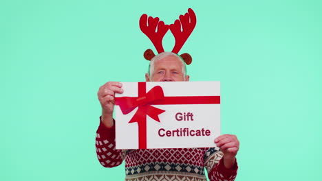 Senior-grandfather-man-in-New-Year-sweater-presenting-card-gift-certificate-coupon-winner-voucher