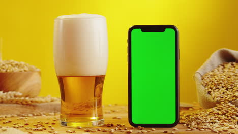 pouring beer into glass with green screen mobile phone and barley