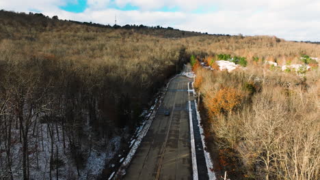 Auto-Fährt-Auf-Leerer-Straße-Durch-Blattlosen-Winterwald,-Sonnig,-Luftaufnahme