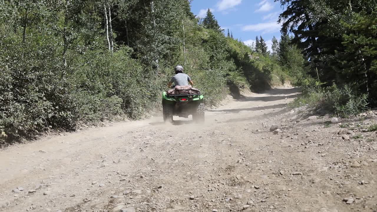 toma en cámara lenta de un ciclista de atv conduciendo su quad en un camino de tierra en las montañas, dejando una gran nube de tierra detrás de él