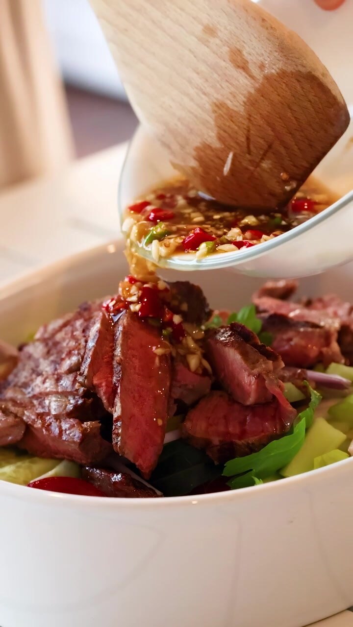 Salad Daging Sapi yang Penuh Warna Disiapkan dengan Saus Pedas di Dapur yang Terang Benderang, Menyoroti Bahan-bahan Segar dan Teknik Kuliner