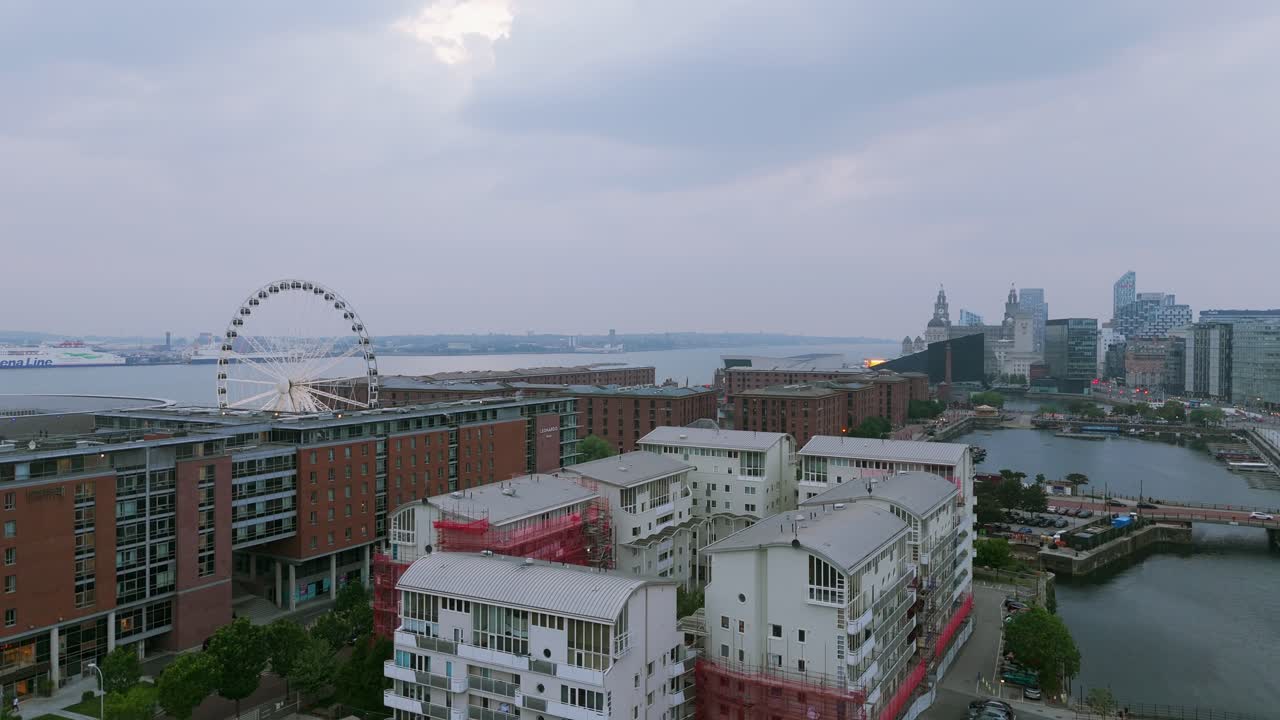Modern apartments on Liverpool waterfront, Ferris Wheel, Pier Head skyline in background, England, UK. Aerial drone descending, copy space