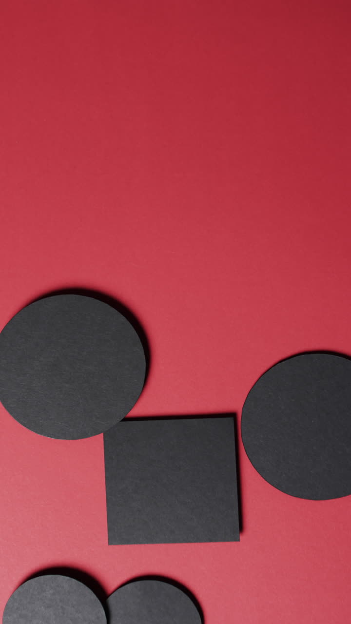 Vertical video of square and circles of black paper and copy space on red background