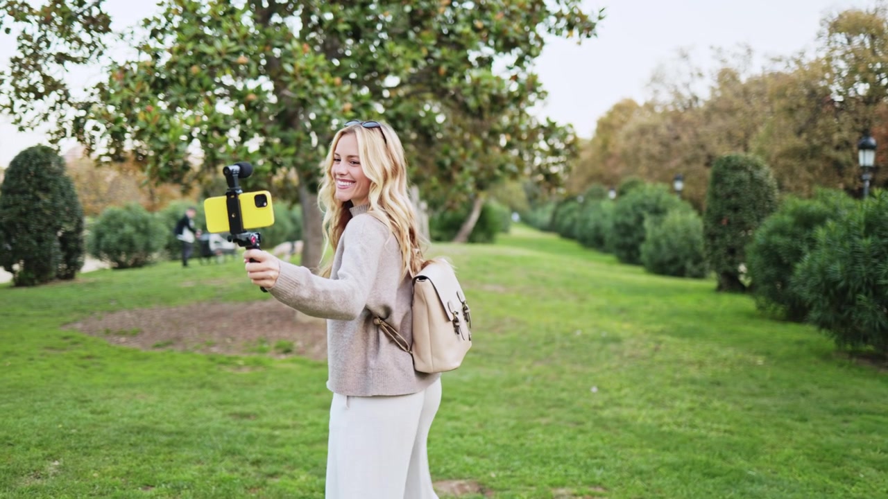 Donna sorridente che registra un video con uno stabilizzatore per smartphone al parco.
