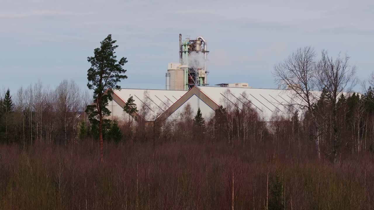 Langsomt, lodret dronebillede, hvor fabriksstrukturen dukker op bag den naturlige skov