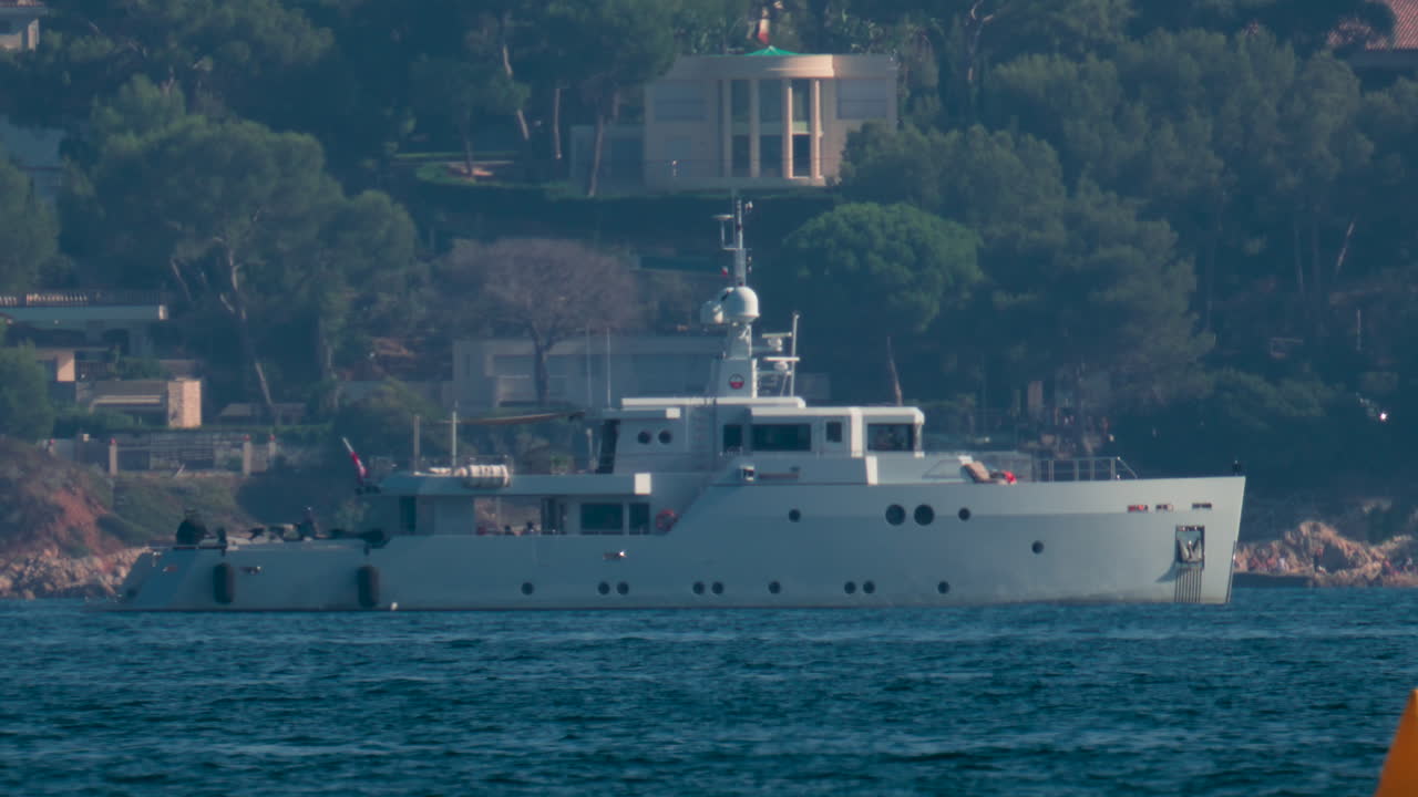 A bright yellow buoy floating on calm blue water with a yacht blurred in the background