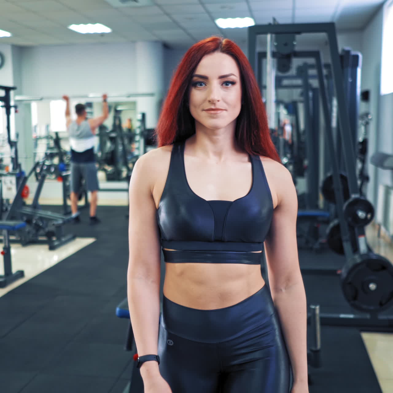 Portrait of a young muscular woman coming into gym. Beautiful athletic woman in sportswear starts her daily workout with dumbbells in modern fitness club.