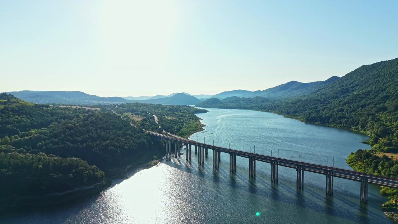 晴れた明るい空の日に、丘と木々に囲まれた川にかかる橋の眺め。